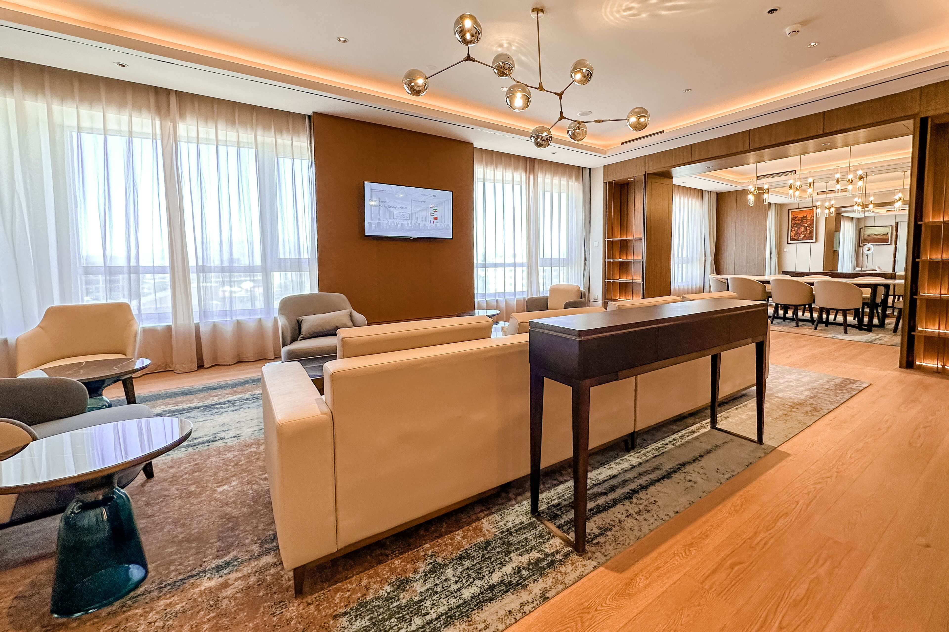 Een moderne hotel lobby met een zithoek, een eettafel en een groot scherm waarop een kaart wordt getoond.