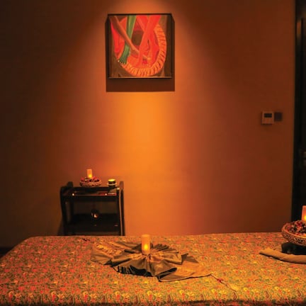 A hotel room with a patterned bedspread, a bedside table with a candle, and a framed artwork on the wall.