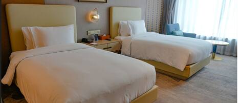 Habitación de hotel con dos camas, una mesita de noche con lámpara, una pequeña mesa y una ventana con cortinas.