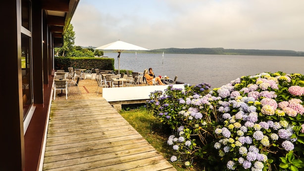 Una terraza de madera con mobiliario exterior y vista a un lago.