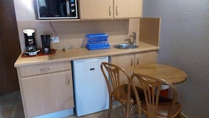 Cocina compacta con microondas, cafetera y lavabo. Se observan armarios de madera y un refrigerador pequeño.