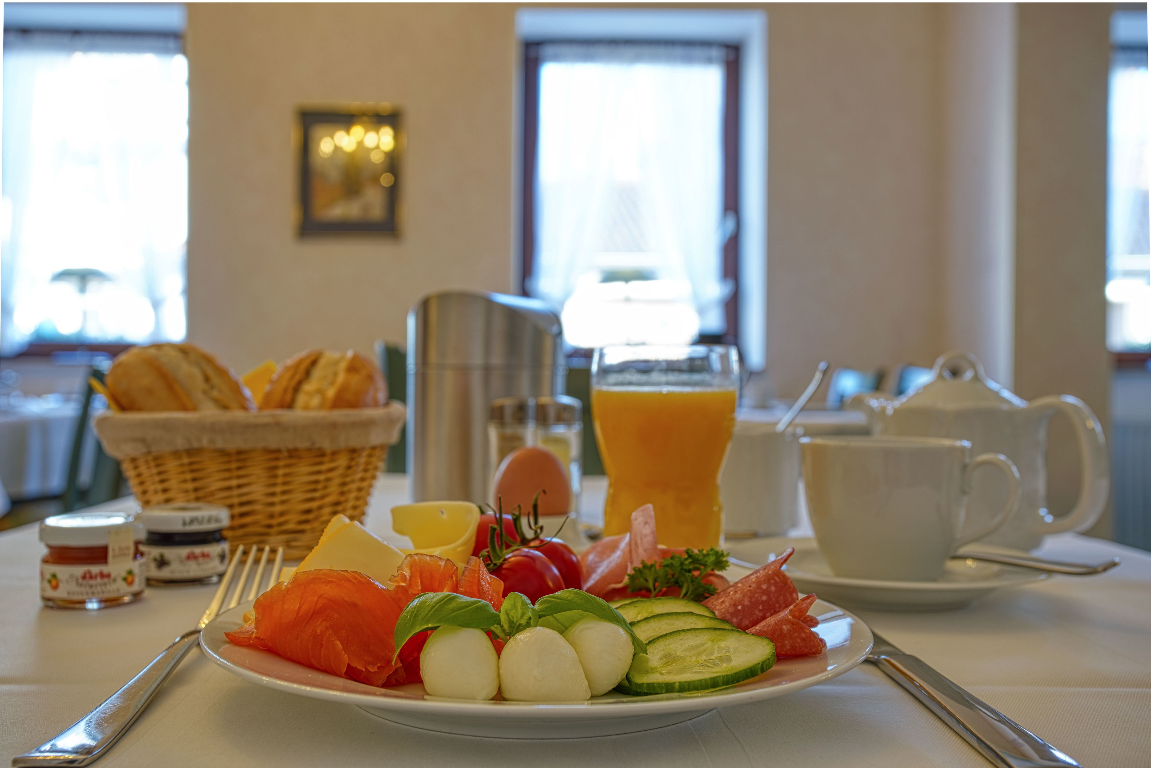Une table mise pour le petit-déjeuner avec une assiette de nourriture, un panier de pain, une carafe et une tasse.