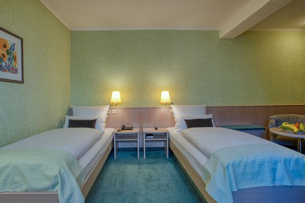 A hotel room with two single beds, a small table with a chair, a lamp, and a painting on the wall. - Hotel Kischers Landhaus (Hannover)