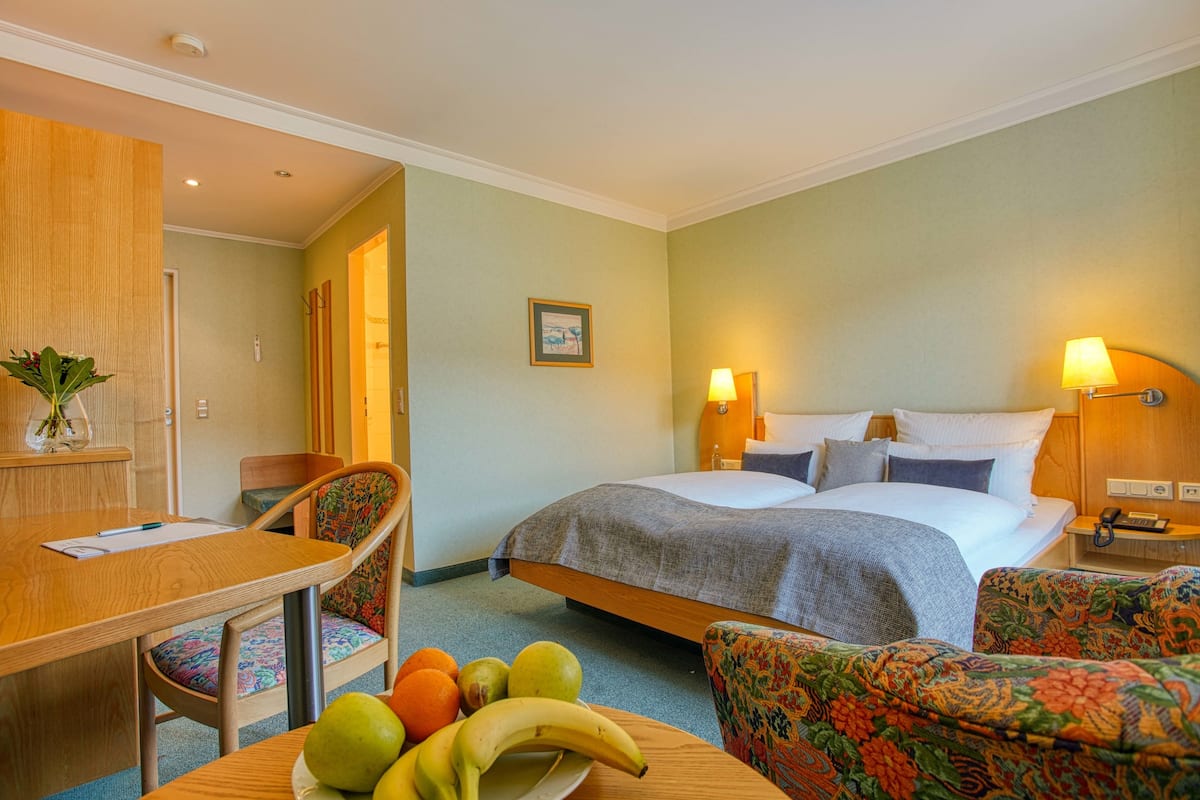 A hotel room with a bed, a desk, a chair, and a table with fruit.