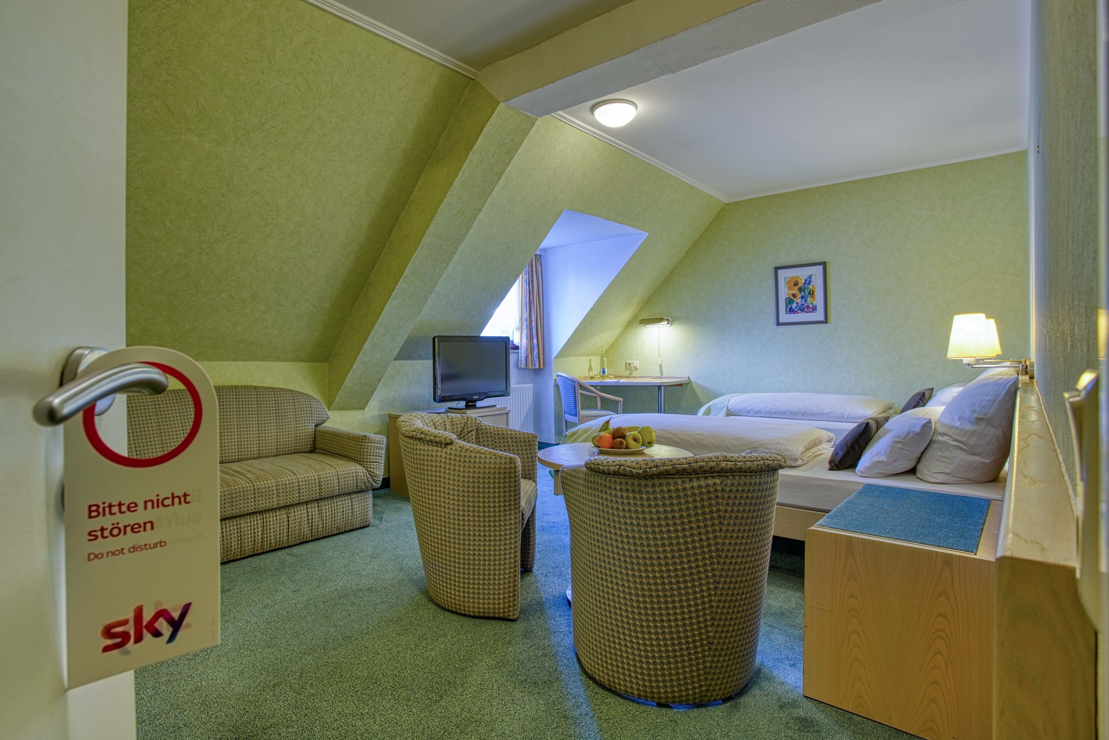 Une chambre d’hôtel comprenant un lit, une télévision, une table à manger et deux chaises en osier.