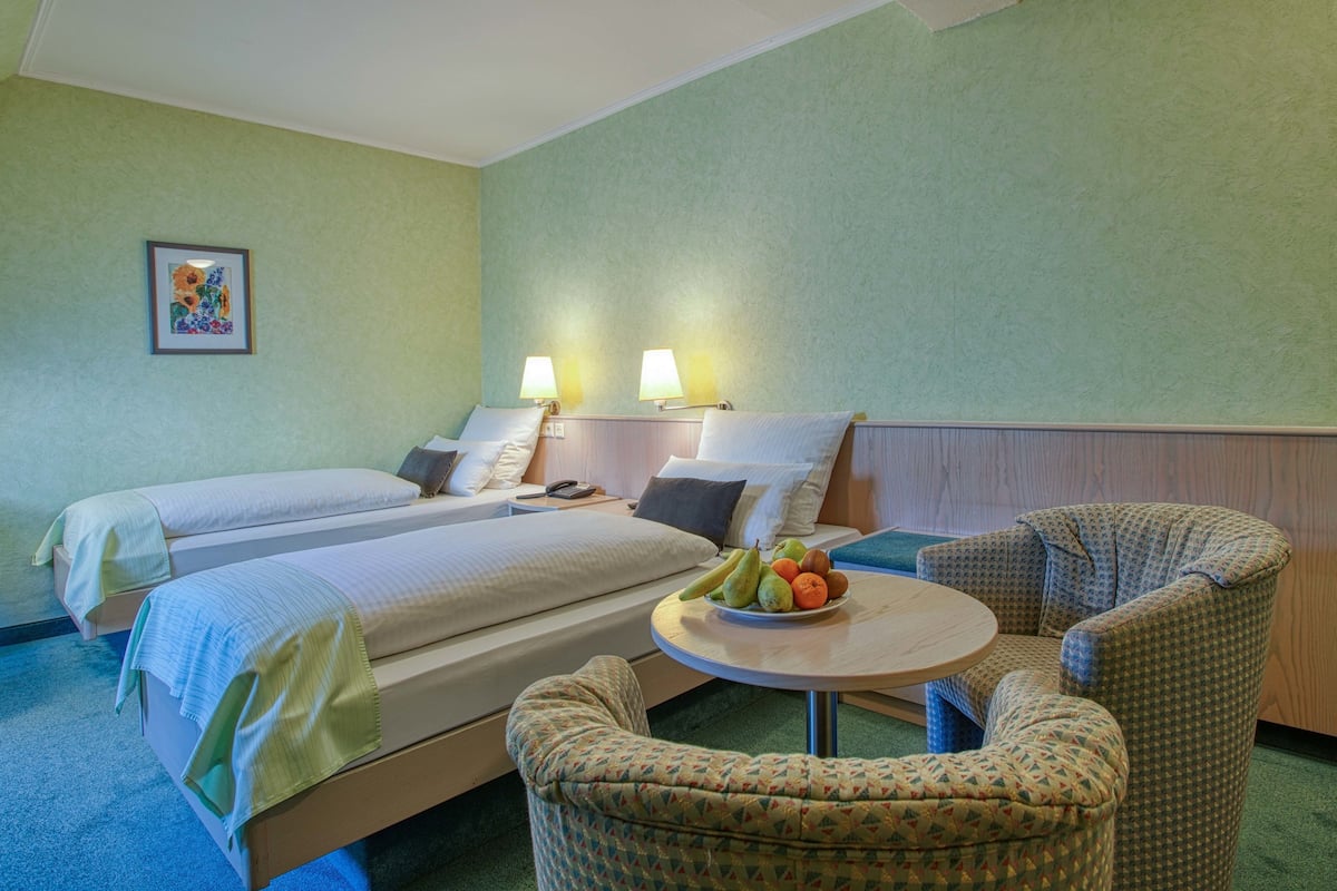 A hotel room with two beds, a round table with fruit, and two lamps.