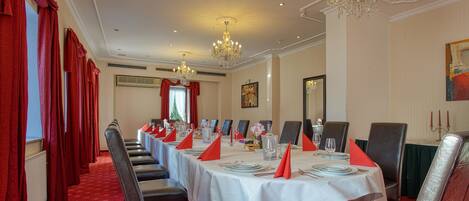 A formal dining room with a long table set for a meal, red curtains, and a chandelier.