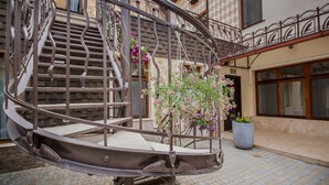 A spiral staircase with a metal railing, surrounded by a building with a checkered facade and a large potted plant. - Shato Luxe Hotel (Odesa)