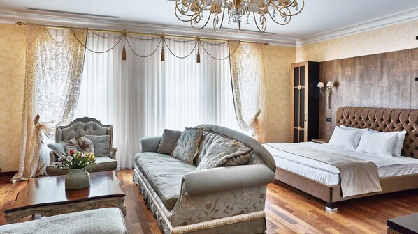 A spacious bedroom with a large bed, a sofa, a chair, and a wooden wardrobe.