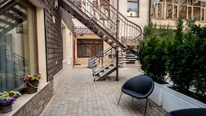 A courtyard with a wrought iron staircase leading to a second-story balcony, surrounded by potted plants and a wicker chair. - Shato Luxe Hotel (Odesa)