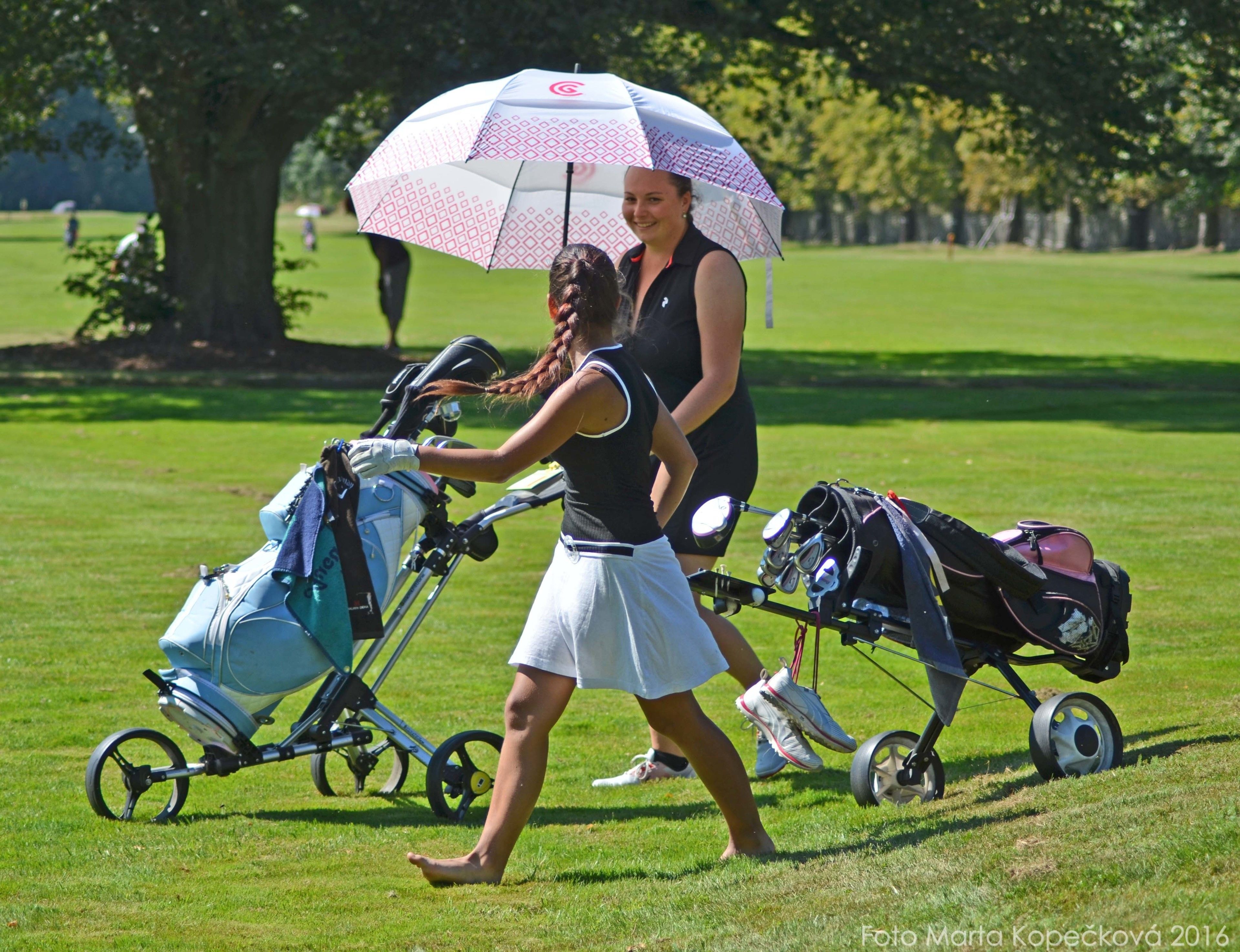 Eine Frau schiebt einen Kinderwagen und trägt eine Golftasche über eine Wiese.