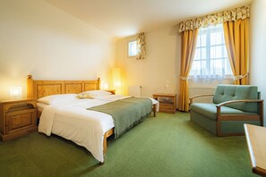 A hotel room with a bed, bedside tables, a chair, a lamp, a window with curtains, and a radiator. - Penzion Černická obora (Sudomerice u Bechyne)