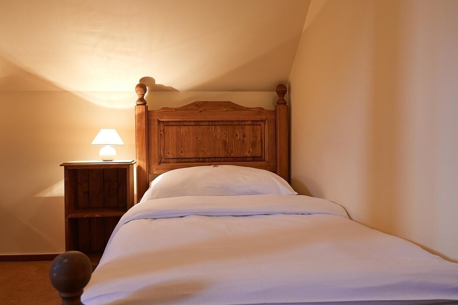 A single bed with a wooden headboard in a room with a sloped ceiling.