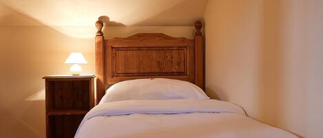A single bed with a wooden headboard in a room with a sloped ceiling.