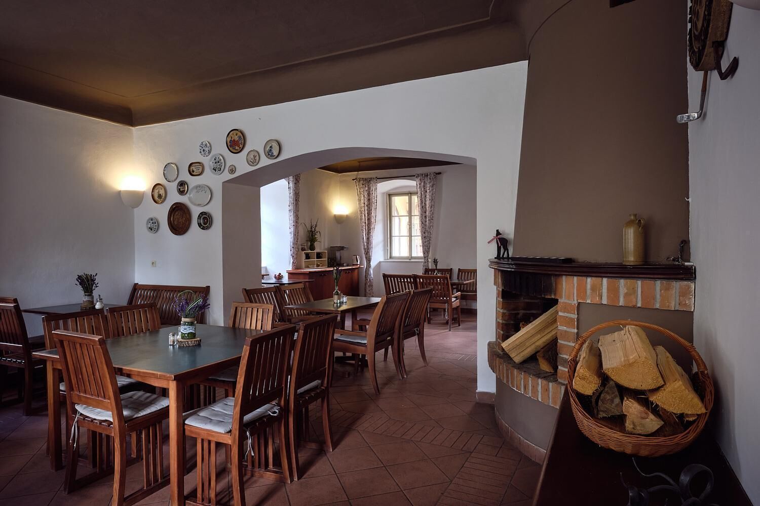 Un comedor con una mesa larga y múltiples sillas, una chimenea con leña, y una cocina visible a través de un arco.
