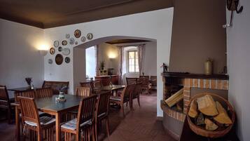Un comedor con una mesa larga y múltiples sillas, una chimenea con leña, y una cocina visible a través de un arco.