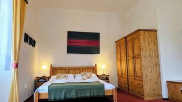 A bedroom with a bed, bedside lamps, a wooden wardrobe, a wall-mounted artwork, and a window with curtains.