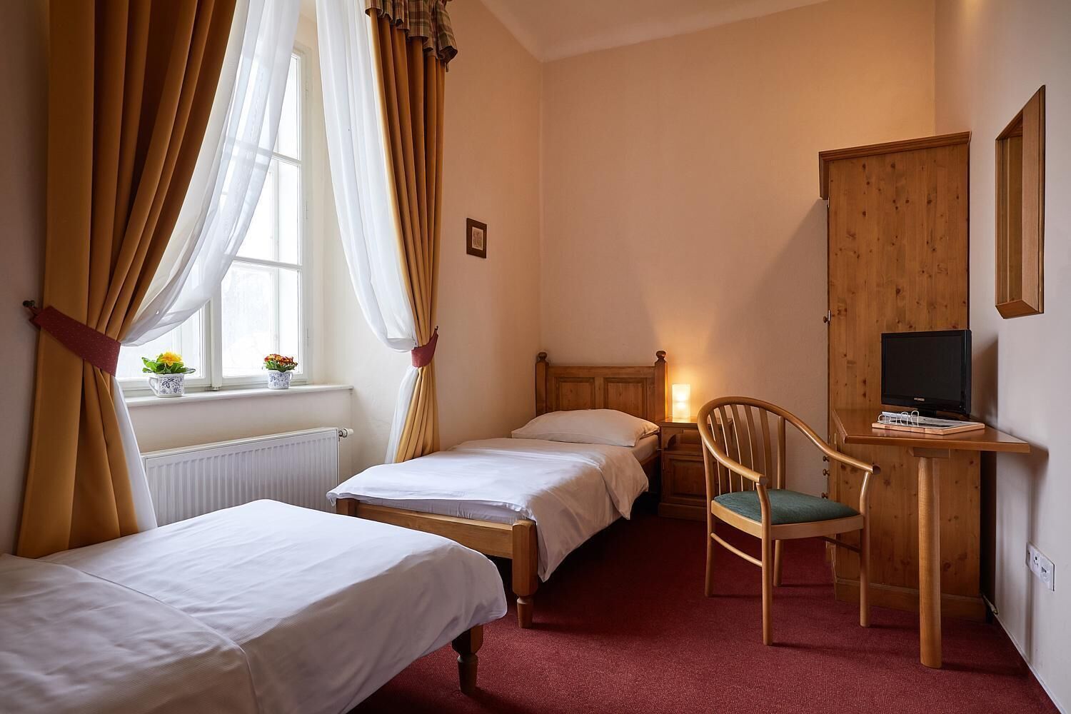 Ein Schlafzimmer mit zwei Einzelbetten, einem Schreibtisch mit Stuhl, einem Fernseher und einem Fenster mit Vorhängen.