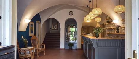 A spacious hallway with a central staircase, a bar area with a view, and a dining setup with wicker chairs.