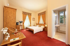 A hotel room with a wooden bed, a desk with a chair, a TV, and a bathroom visible through an open door. - Penzion Černická obora (Sudomerice u Bechyne)