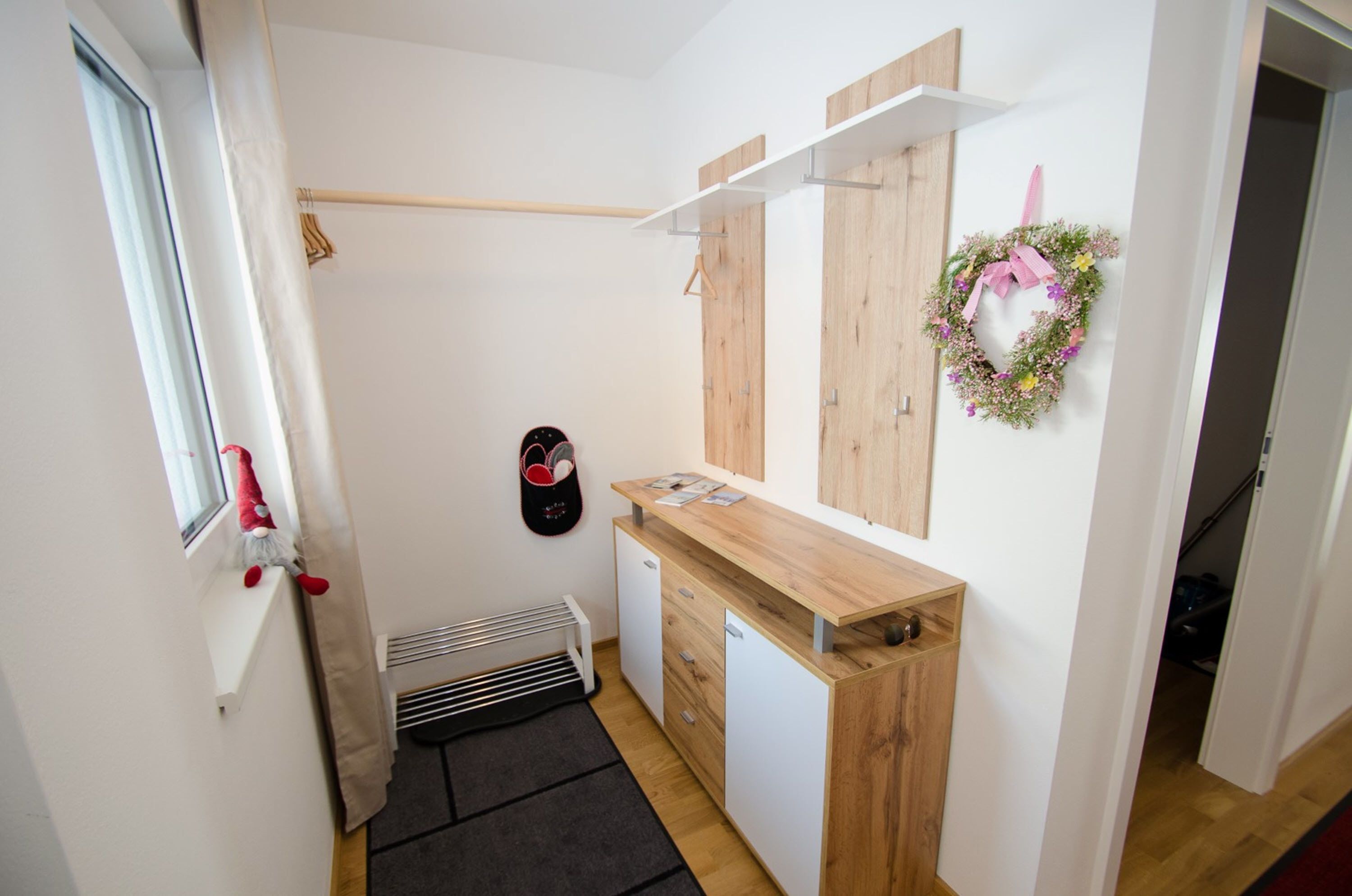 Un baño pequeño con tocador de madera, perchero, radiador y una ventana con un peluche rojo.