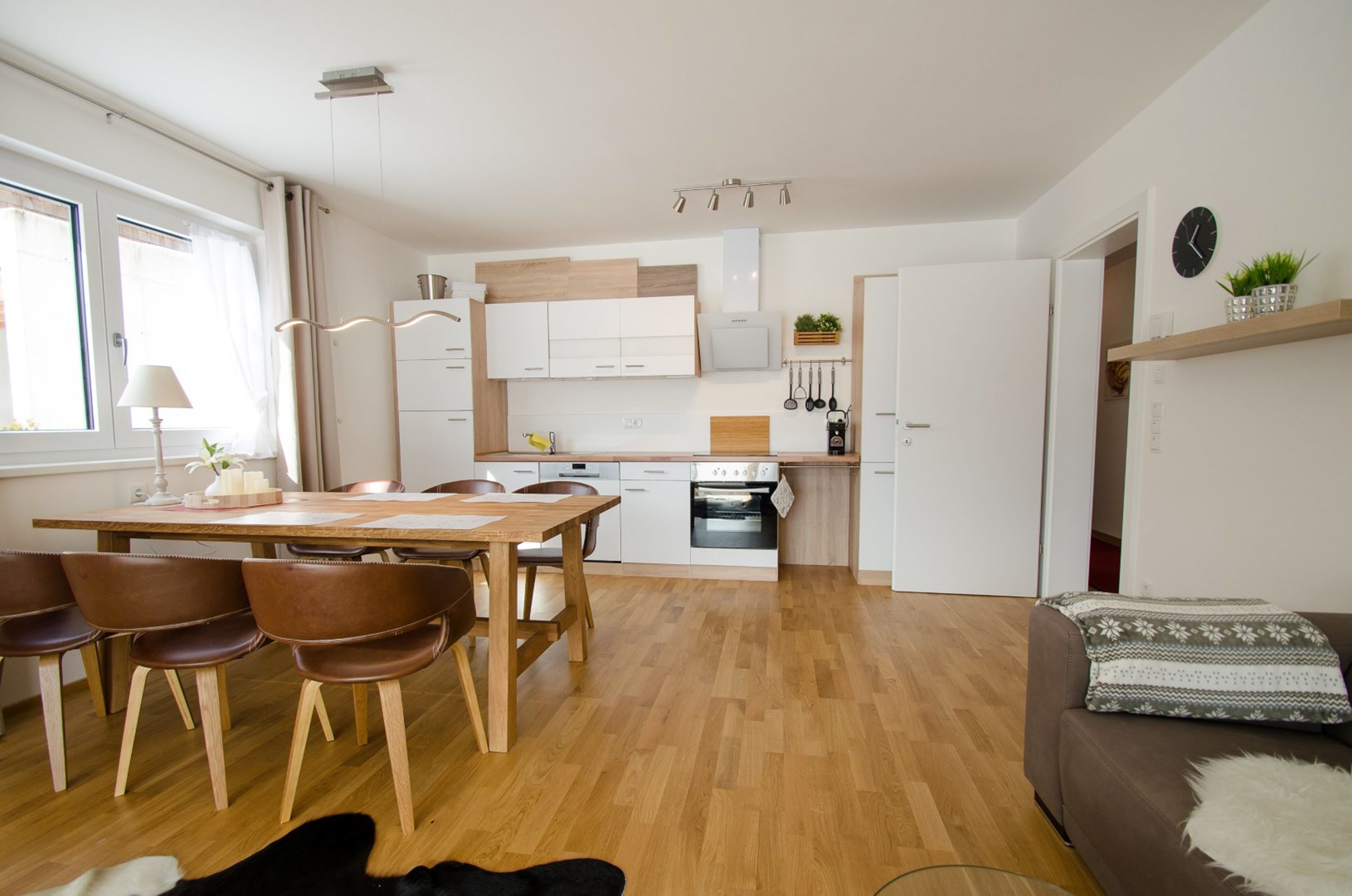 A modern kitchen with wooden cabinets, a dining area with a table and chairs, and a cozy living space with a sofa.