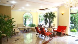 A spacious lobby with a beige sofa, red chairs, a coffee table, and a large potted plant. - Hotel Dona Beja (Araxá)