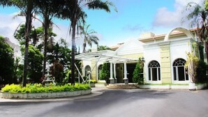 A hotel with a covered entrance, palm trees, and a fountain. - Hotel Dona Beja (Araxá)