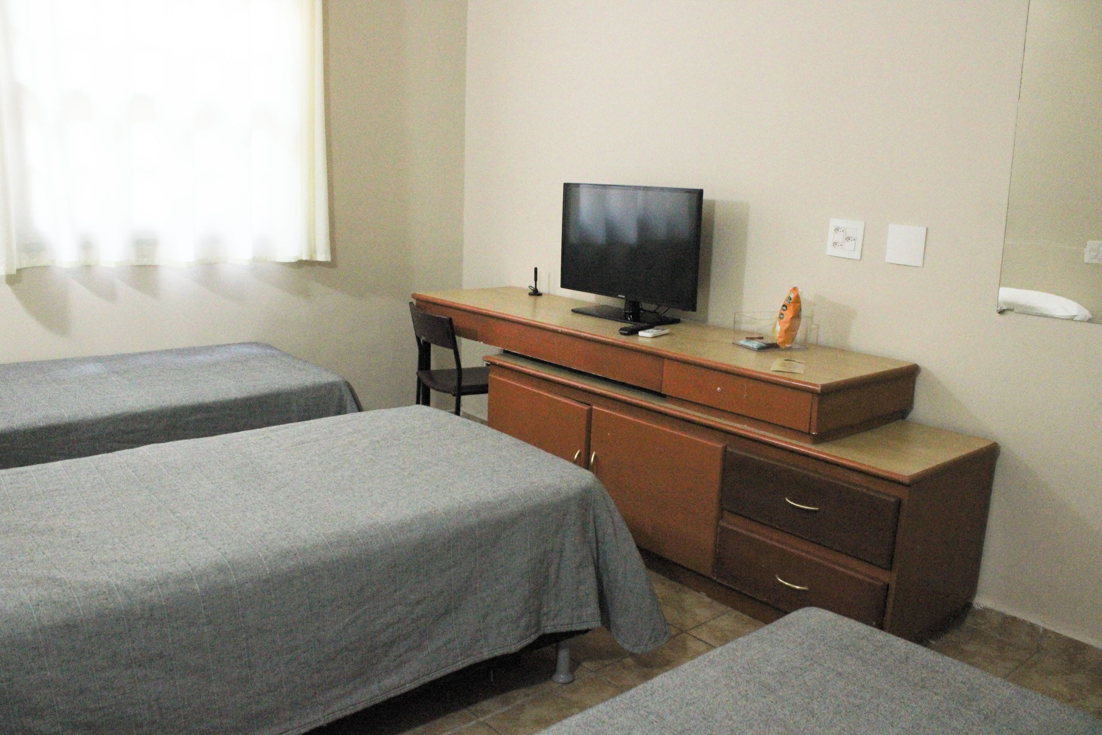A room with two single beds, a desk with a television, and a cabinet.