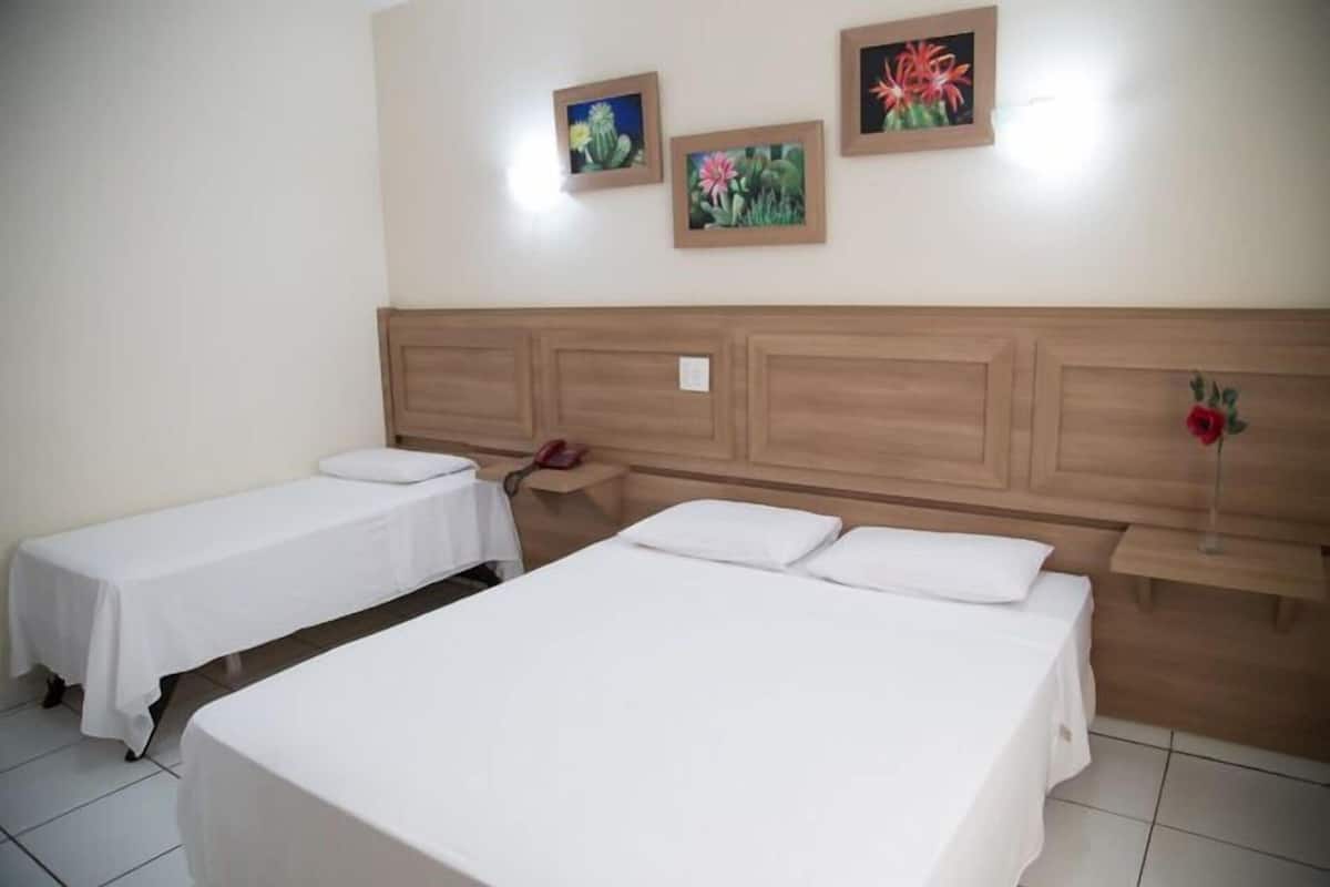 Ein Hotelzimmer mit zwei Einzelbetten, einem Holz-Kopfteil und drei gerahmten Blumenbildern an der Wand.