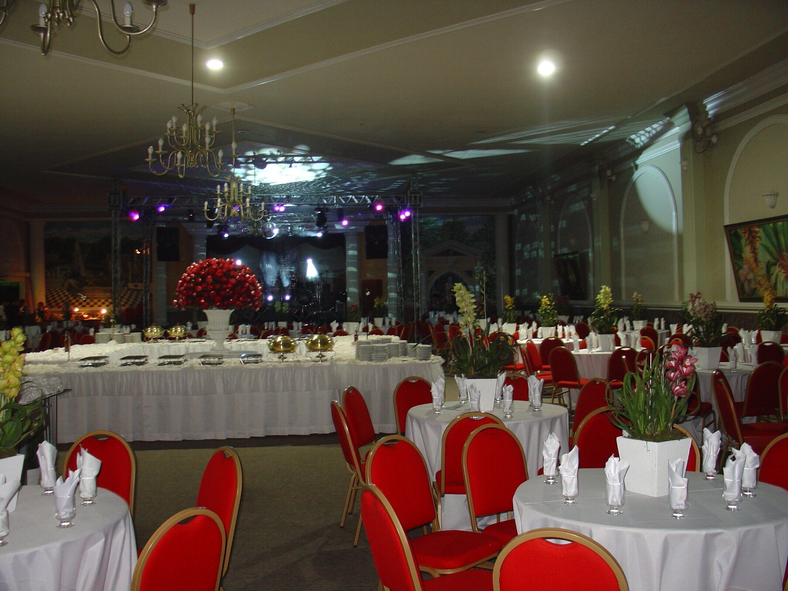Un salón de banquetes con mesas redondas, sillas rojas y manteles blancos.