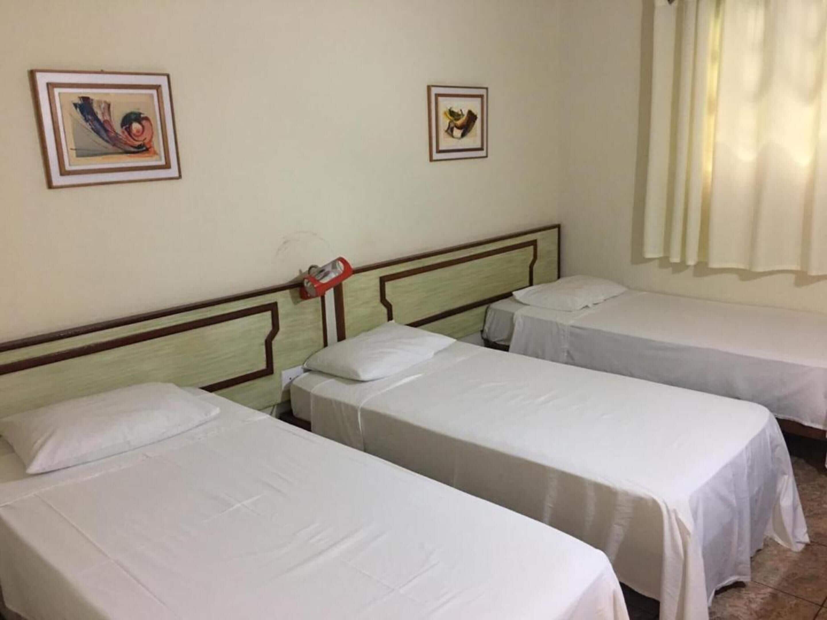 Habitación de hotel con tres camas individuales, cabecera de madera y dos cuadros en la pared.