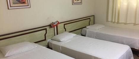 Habitación de hotel con tres camas individuales, cabecera de madera y dos cuadros en la pared.
