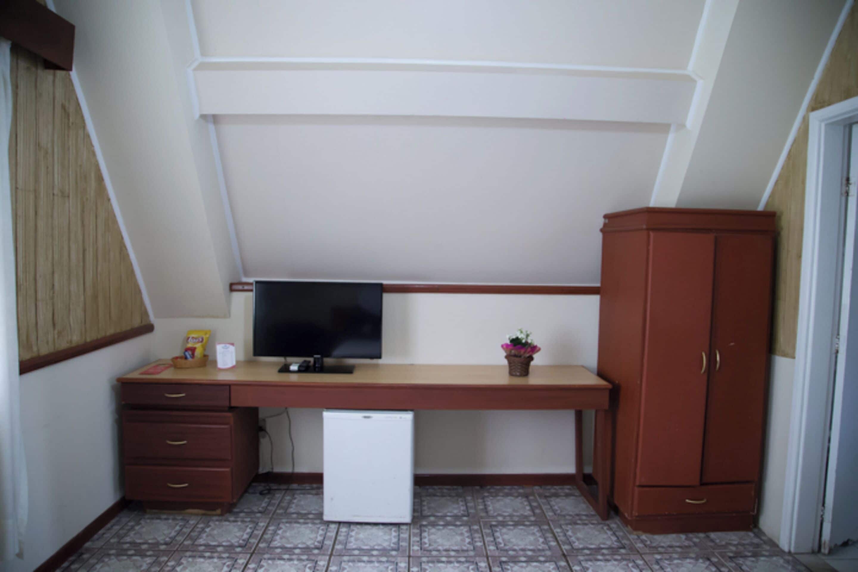 Ein kleiner, kompakter Raum mit Schreibtisch, Fernseher, kleinem Kühlschrank und Schrank.