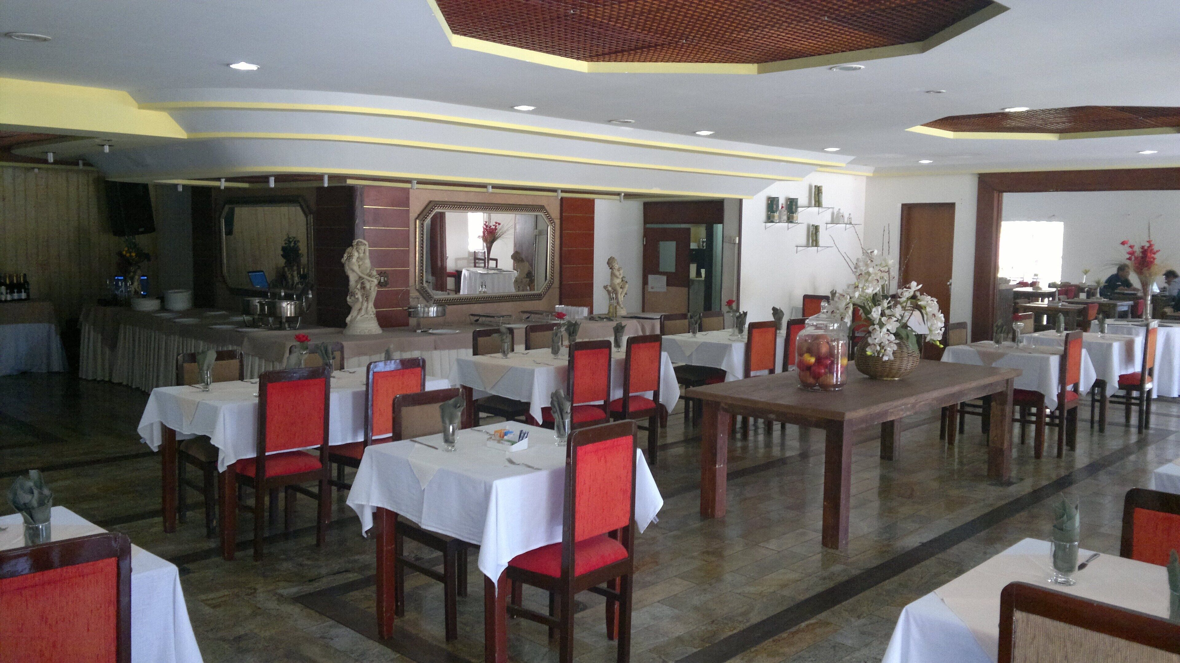 A restaurant with multiple tables and chairs, a bar area, and decorative statues.