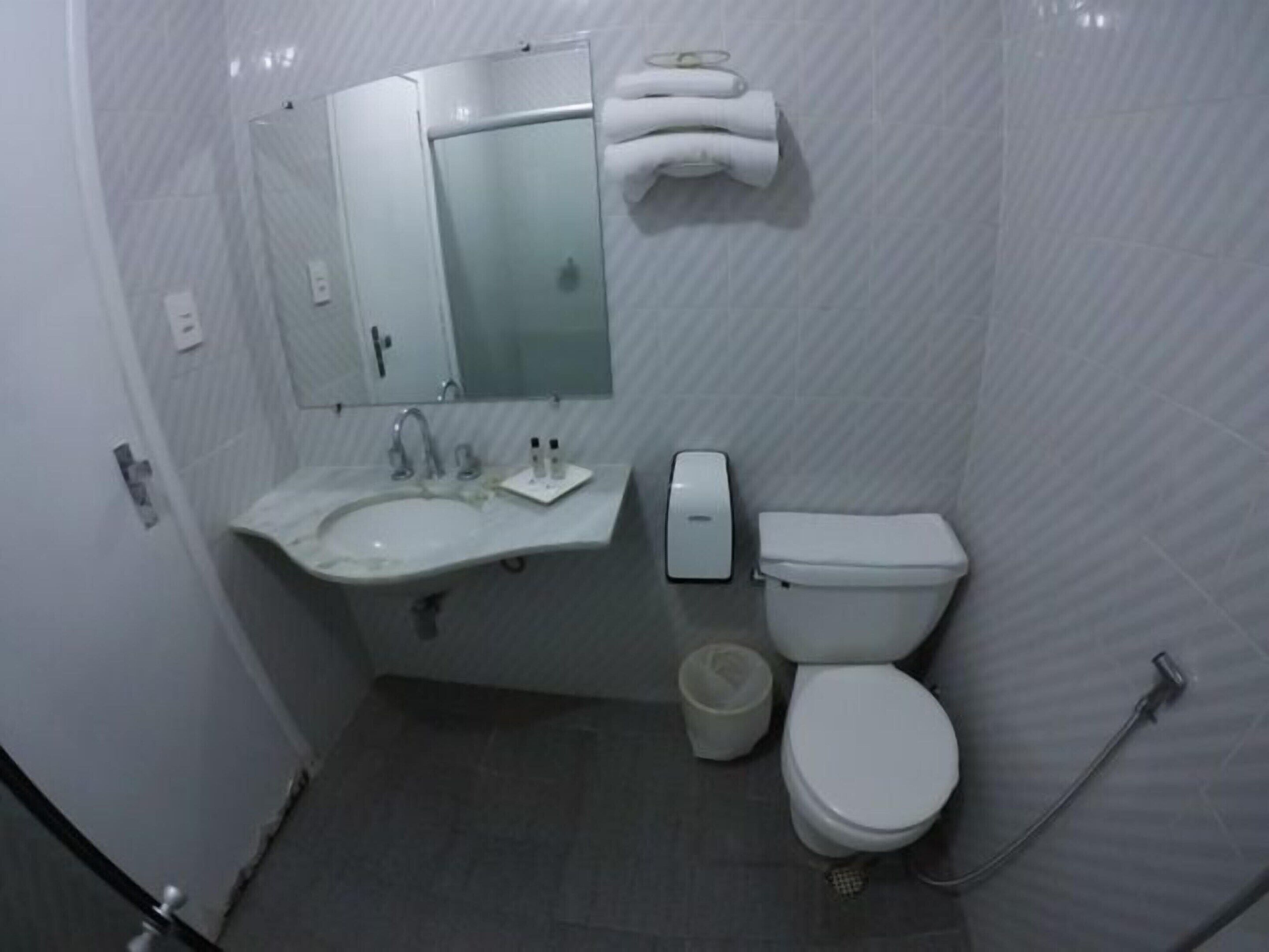 A small, compact bathroom with a sink, mirror, toilet, and hand dryer.