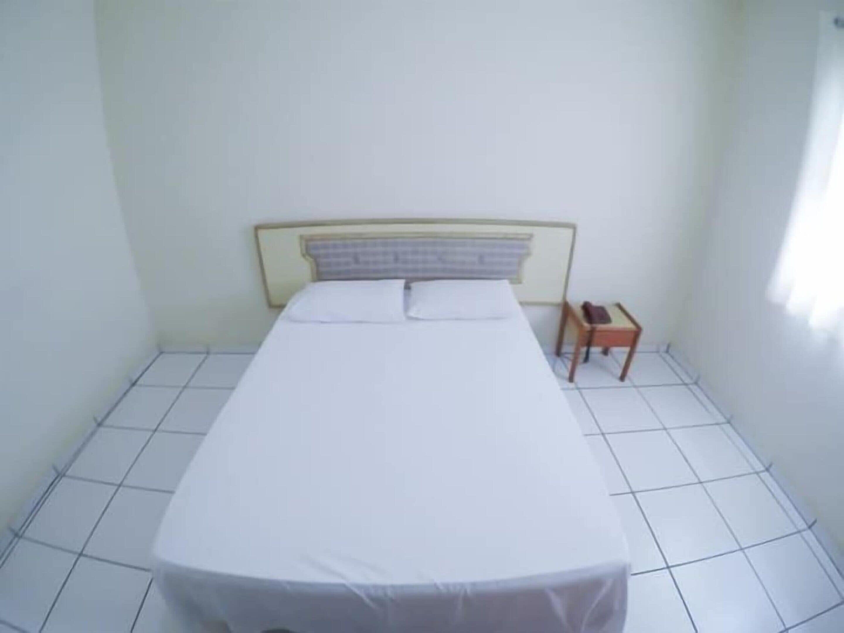 A small, clean room with a single bed, a nightstand, and a chair.