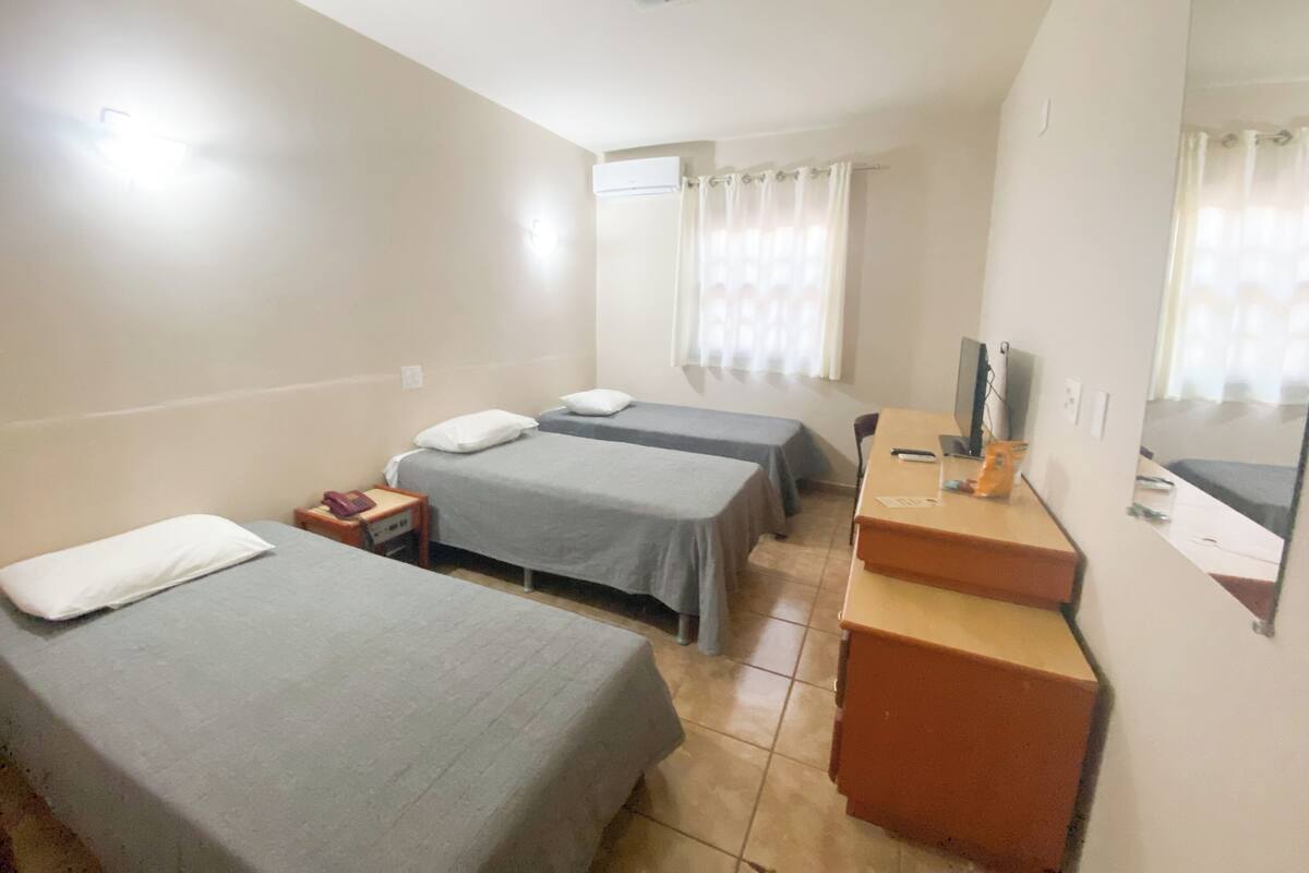 Ein Hotelzimmer mit zwei Einzelbetten, einem Schreibtisch mit Computer, einem Fernseher und einem kleinen Tisch.