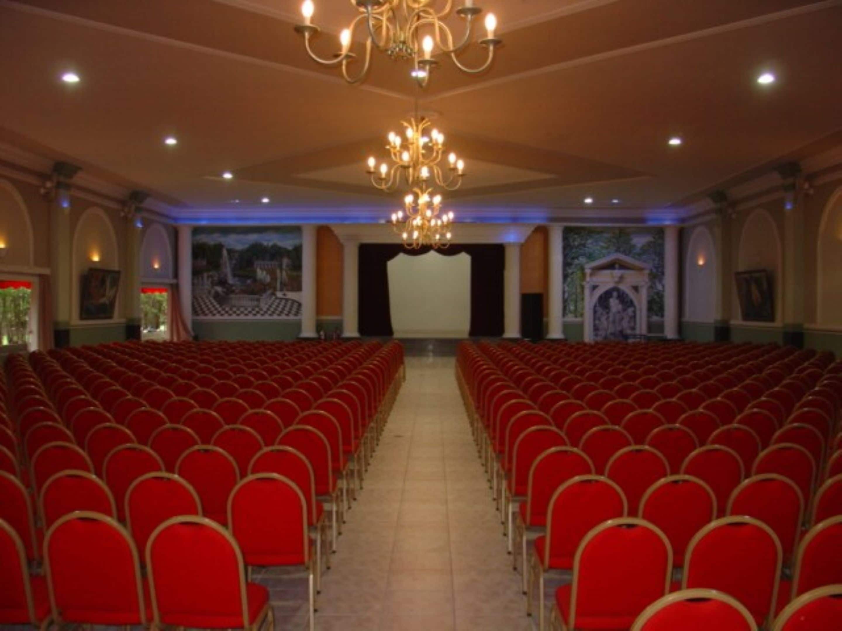 A theater with rows of red chairs, a stage, and a chandelier.