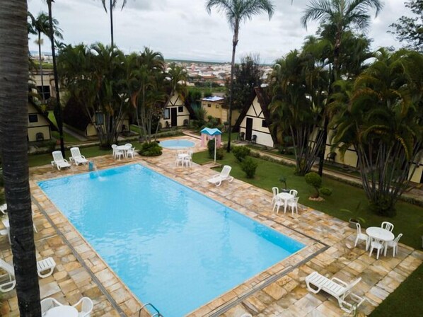 A rectangular swimming pool with a tiled deck, surrounded by white lounge chairs and a small garden area with palm trees. - Hotel Dona Beja (Araxá)