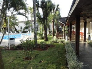 A pool area with lounge chairs, a covered patio, and a small garden with palm trees. - Hotel Dona Beja (Araxá)