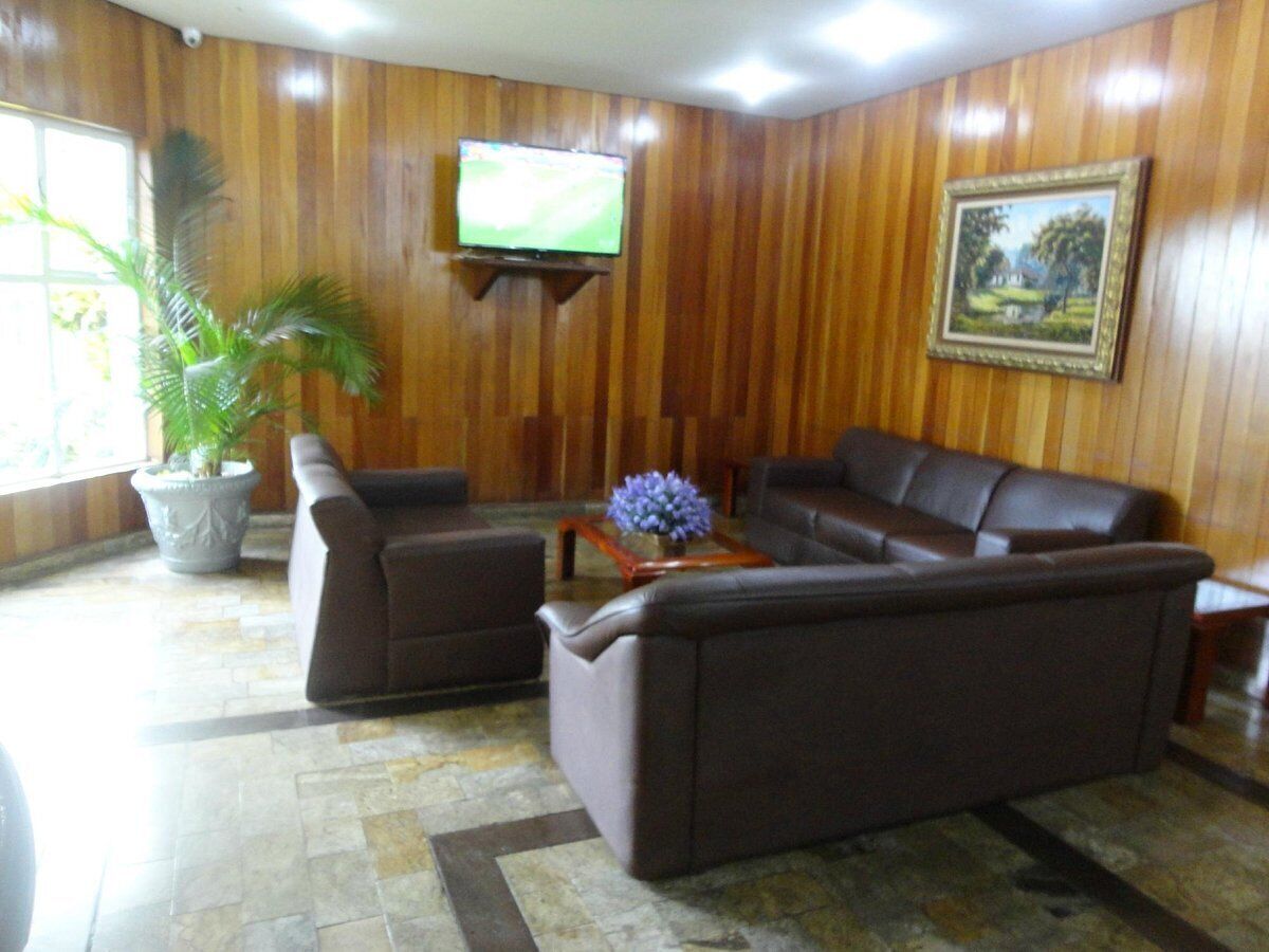 Ein Zimmer mit einer holzverkleideten Wand, einem Fernseher über einem braunen Ledersofa, einer Topfpflanze und einem gerahmten Bild.