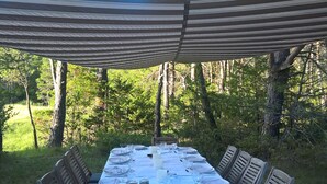 Een buiten eetgedeelte met een tafel voor zes personen, omringd door houten stoelen, onder een gestreepte luifel.