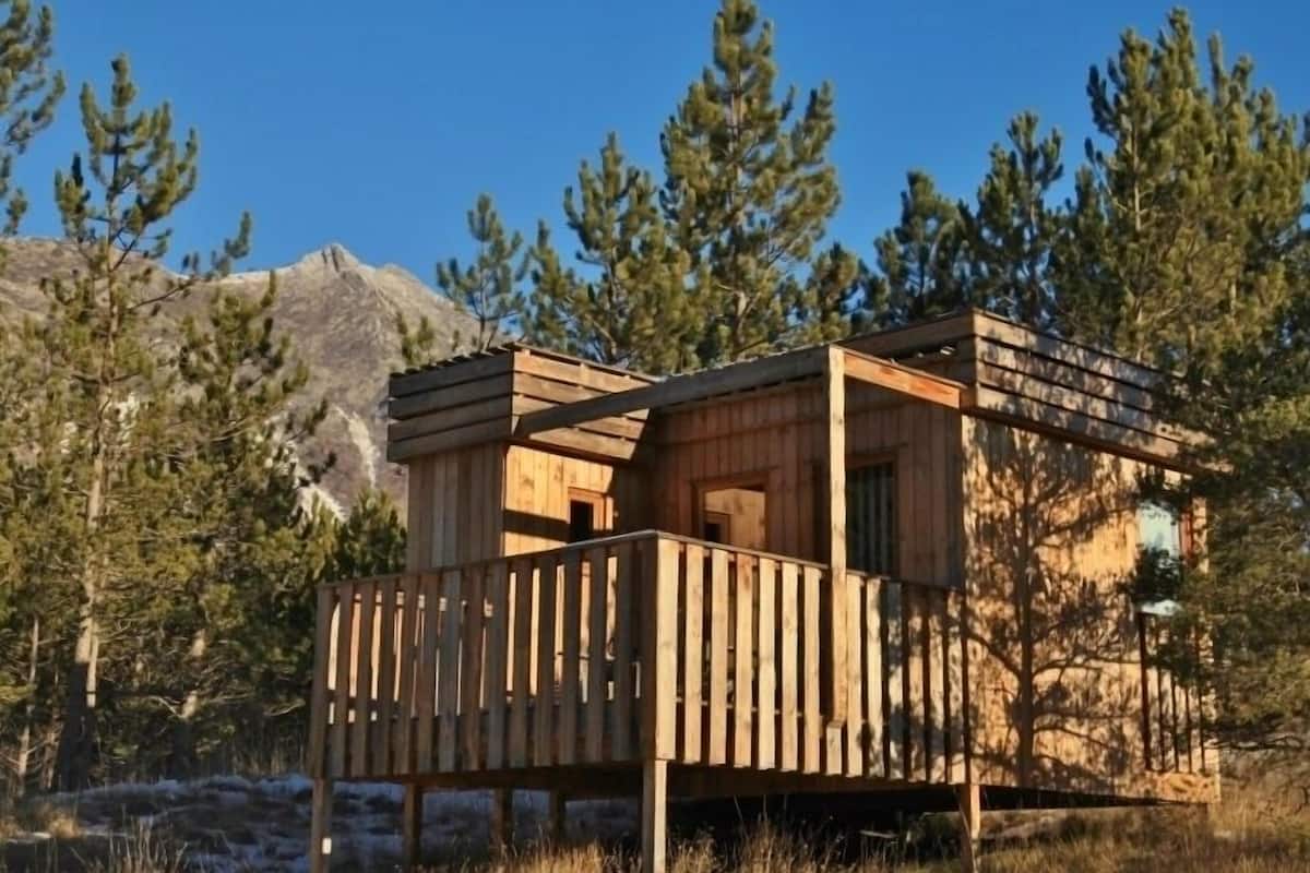 Een houten chalet met een balkon, omringd door bomen en een berg op de achtergrond.