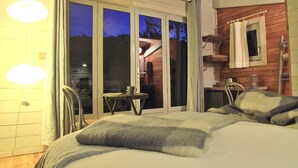 Een slaapkamer met een bed, kussens, een tafel met een kopje en een stoel.