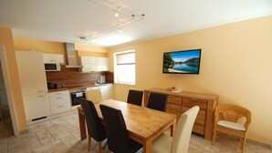 A compact kitchen with modern appliances, a dining area with a wooden table and chairs, and a large window providing natural light. - Penthouses Zell am See (Zell am See)