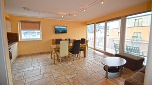 A dining area with a table and chairs, a television on the wall, and a balcony with a view of buildings. - Penthouses Zell am See (Zell am See)