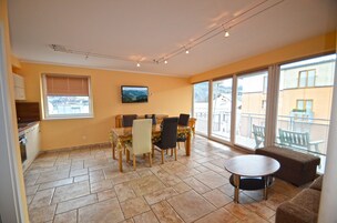 A dining area with a table and chairs, a television on the wall, and a balcony with a view of buildings.