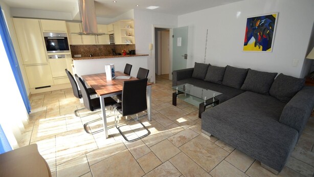 A modern living room with a grey sofa, a glass coffee table, and a dining area with a wooden table and chairs. - Penthouses Zell am See (Zell am See)