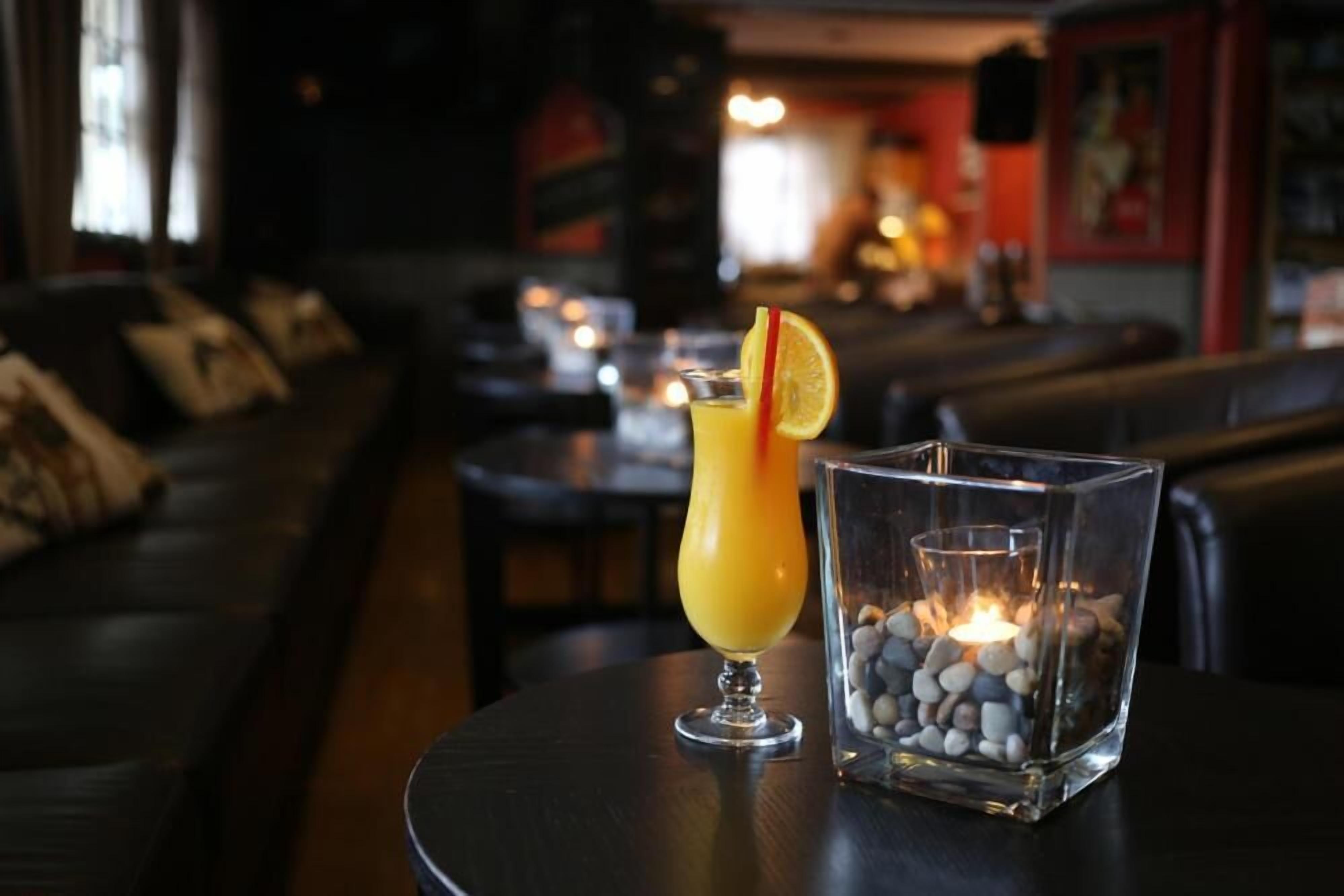 A bar area with a round table, a glass candle holder with stones, and a sofa in the background.